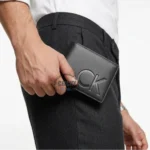 Close-up of a man’s hand holding a black leather wallet with an embossed CK logo.