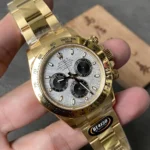 Gold Rolex Daytona wristwatch with a silver dial, black subdials, and a gold tachymeter bezel, held in a hand.