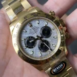 Close-up of a gold Rolex Daytona chronograph on a metal bracelet, featuring a textured silver dial with three black subdials and a tachymeter bezel.