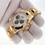 Gold Rolex Daytona wristwatch with three black subdials, held by a gloved hand.