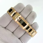 Gold Rolex-style link bracelet with a crown-embossed clasp held on a gloved hand, close-up detail of the jewelry piece.