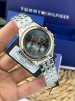 1781976-original-tommy-hilfiger-watch-women-silver-metal-ari-egypt_100 Tommy Hilfiger wristwatch with metallic band, teal dial, rose-gold bezel, and diamond-studded rim; brand logo visible with a product tag attached.