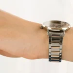 Close-up of a silver metal wristwatch worn on a forearm, showing the watch face and linked band.