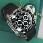 Close-up of a Rolex Daytona watch with a black dial, diamond hour markers, and a black rubber strap on a green background.