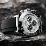 Close-up of a silver Rolex Daytona chronograph with a black bezel and rubber strap resting on a rocky surface.