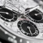 Close-up of a watch dial with three black subdials, silver hands, and a red 'DAYTONA' inscription in focus on a textured surface.