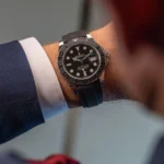 Man wearing a black Rolex Yacht-Master wristwatch with a rubber strap on a blue suit sleeve.