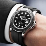 Close-up of a Rolex Yacht-Master watch on a man's wrist with a black dial, silver case, and black rubber strap
