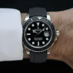 Rolex Yacht-Master wristwatch with black dial, silver case, and black rubber strap on a wrist with a white shirt cuff visible on the left.