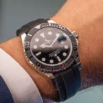 Close-up of a Rolex Yacht-Master on a wrist, black bezel, gradient dial, and date magnifier over the 3 o'clock window on a rubber strap.