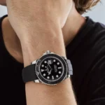 Close-up of a man's wrist wearing a black Rolex Submariner dive watch with a black rubber strap.