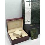 Audemars-Piguet-watch-box-packaging Open burgundy watch box with cream lining and a beige cushion, labeled Audemars Piguet, surrounded by black and white gift boxes.