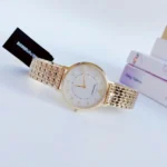 Gold-tone women's wristwatch with crystal hour markers and white dial, linked bracelet, tag attached.