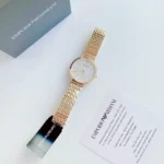 Gold-tone Emporio Armani wristwatch with a metal link bracelet, shown beside its gray box and warranty card on a light surface.