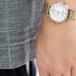 Gold-toned wristwatch with a white dial and diamond hour markers on a plaid shirt sleeve.