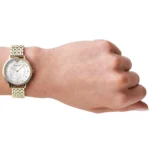 Gold-tone wristwatch with a metal link band worn on a light-skinned wrist. White dial with small markers and gold hands, photographed from the side.
