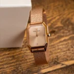 ar11347-emporio-armani-watch-square-women-rose-gold-dial-mesh-stainless-steel-metal-rose-gold-strap-quartz-battery-analog-gioia_30 Rose gold Emporio Armani watch with a mesh band resting beside a white box on a wooden surface, close-up view of the timepiece.