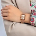 ar11347-emporio-armani-watch-square-women-rose-gold-dial-mesh-stainless-steel-metal-rose-gold-strap-quartz-battery-analog-gioia_300 Rose-gold wristwatch with a mesh band worn on a woman’s left wrist, beige coat nearby.