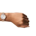 Rose-gold metal wristwatch on a brown-skinned wrist with a white dial and diamond markers.