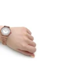 Rose-gold wristwatch on a left hand with a jeweled white dial and crystal accents.