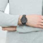 ar1452-emporio-armani-watch_300 Person with arms crossed wearing a dark metal chronograph watch on the left wrist over a light gray sweater, close-up view