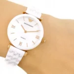 ar1486-emporio-armani-watch-ceramica-women-mother-of-pearl-white-dial-ceramic-strap-quartz-battery-analog-gianni-t-bar_9 White ceramic Emporio Armani wristwatch with gold hands and Roman numeral markers on a wrist.