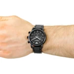 Black metal chronograph wristwatch worn on a man's left wrist with a metal band.