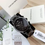 Black Emporio Armani chronograph watch with a metal bracelet, displayed on a box with warranty booklet.