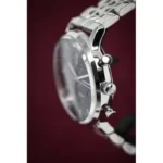 Close-up of a silver wristwatch with crown and pushers on a dark burgundy background.