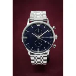 Silver stainless steel chronograph wristwatch with a dark blue dial and three subdials, Emporio Armani branded face against a burgundy background.