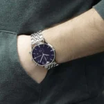 Silver metal wristwatch with a dark blue dial on a person's wrist, showing white hands and markers.