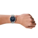 Silver stainless-steel wristwatch with a blue dial on a person's left wrist, showing chronograph subdials and a metal bracelet.