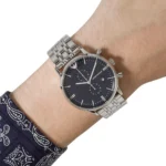 Silver metal wristwatch with a black dial on a man's wrist, featuring chronograph subdials and the Armani logo.
