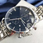 Close-up of a stainless steel chronograph wristwatch with a dark blue face and date window.