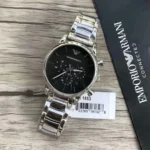 Silver Emporio Armani wristwatch with a black dial and stainless steel link band on a wooden surface, next to a barcode tag and box edge.