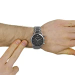 Men's silver metal wristwatch with a black dial on a wrist as another hand touches the band.