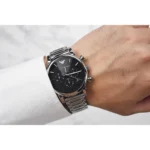 Silver stainless steel wristwatch with a black dial on a forearm wearing a white shirt cuff (Emporio Armani).