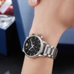 Silver-tone stainless steel wristwatch with a black chronograph dial on a person's wrist.