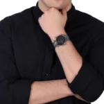 Person in a black shirt rests his chin on his hand, showing a silver wristwatch with a black dial on his left wrist.