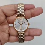 Rose-gold Emporio Armani wristwatch held in hand, with a white dial and Roman numeral markers (III, VI, IX, XII).