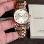 Gold-tone Emporio Armani wristwatch in plastic wrap, held above an instruction booklet.