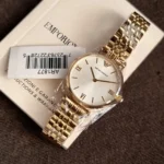 Gold Emporio Armani wristwatch with a metal link bracelet resting on a white box, barcode tag visible nearby.