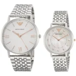 Two Emporio Armani watches with silver metal bands: a larger men's watch with a white dial and rose-gold Roman numerals, and a smaller women's watch with a mother-of-pearl dial and crystal hour markers.