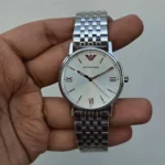 Silver Emporio Armani wristwatch with a white dial and a metal link bracelet, showing Roman numerals at 3, 6, and 9 o'clock with minimal indices and the brand logo at the top edge of the dial.
