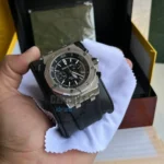 audemars-piguet-automatic-watch-balck-dial-rubber-strap-men-high-premium-quality_7 Close-up of an Audemars Piguet-style stainless steel chronograph watch with a black dial and silver bezel, mounted on a black rubber strap over a white cleaning cloth in a presentation box.