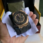 audemars-piguet-royal-oak-offshore-chronograph-26401RO.OO.A002CA.02-balck-dial_3 Gold-toned chronograph wristwatch with black dial and rubber strap held over a white cleaning cloth.