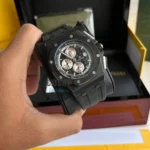 audemars-piguet-watch-battery-diver-for-men_2 Black chronograph wristwatch with an octagonal bezel and screw accents held in a hand, box visible in the background, rubber strap