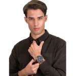 Man in a black button-down shirt adjusts a large black wristwatch on his left wrist, looking at the camera.