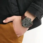 Close-up of a left wrist wearing a large dark metal chronograph watch with a brown leather strap and multiple subdials.
