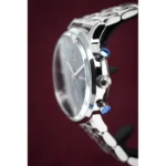 Close-up of a silver wristwatch with blue pushers and crown against a burgundy background.